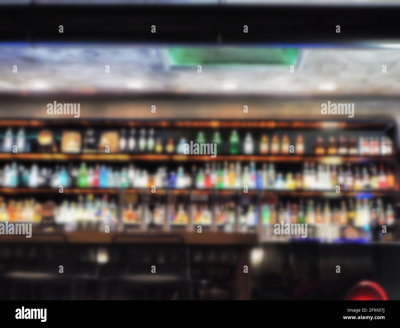 Blurred shot of a bar showing counters full of various drinks and chairs near a wooden table Stock Photo