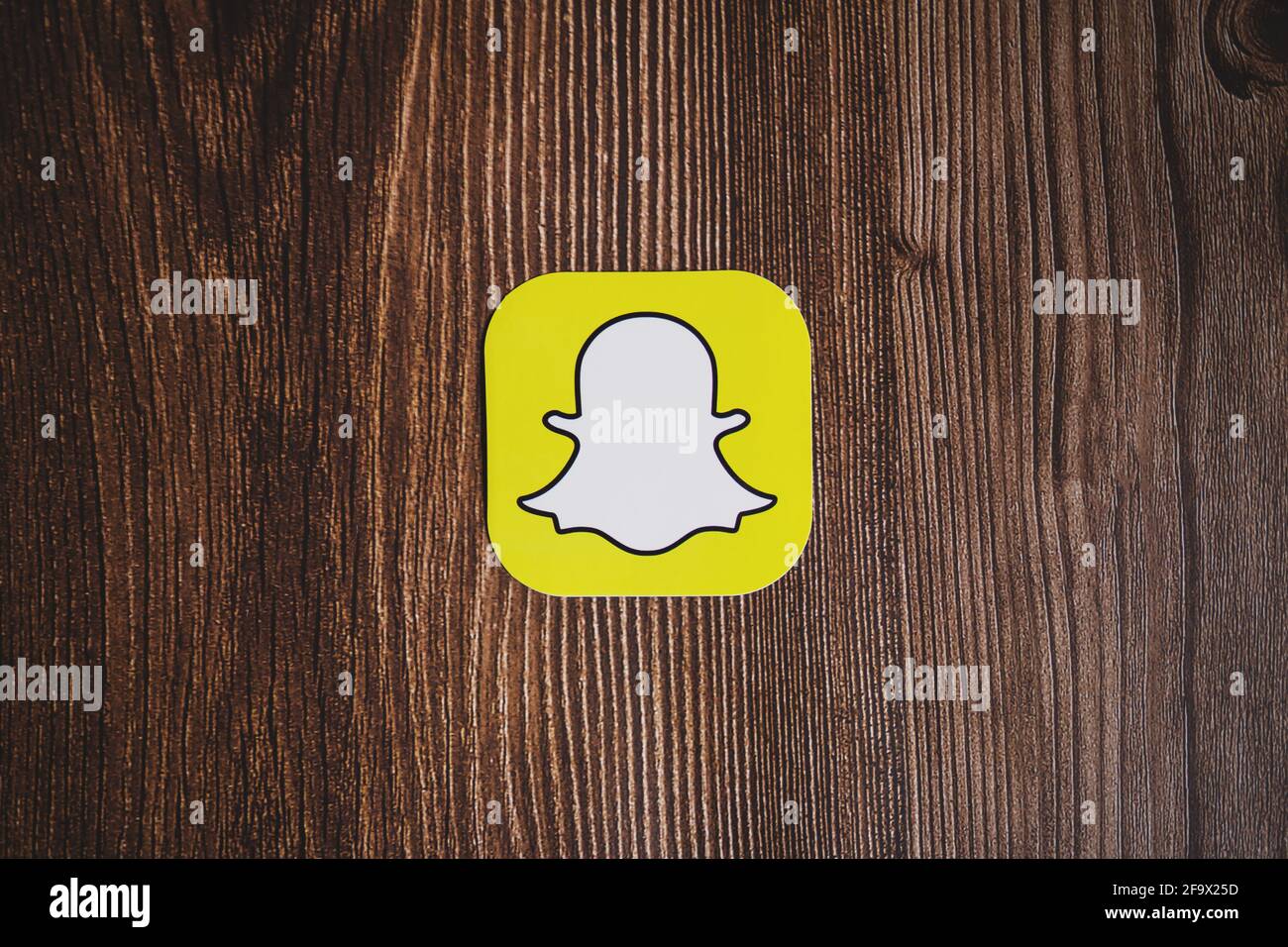 SWANSEA, UK - MARCH 12, 2021: Snapchat yellow logo printed on paper centrally placed on wooden background Stock Photo