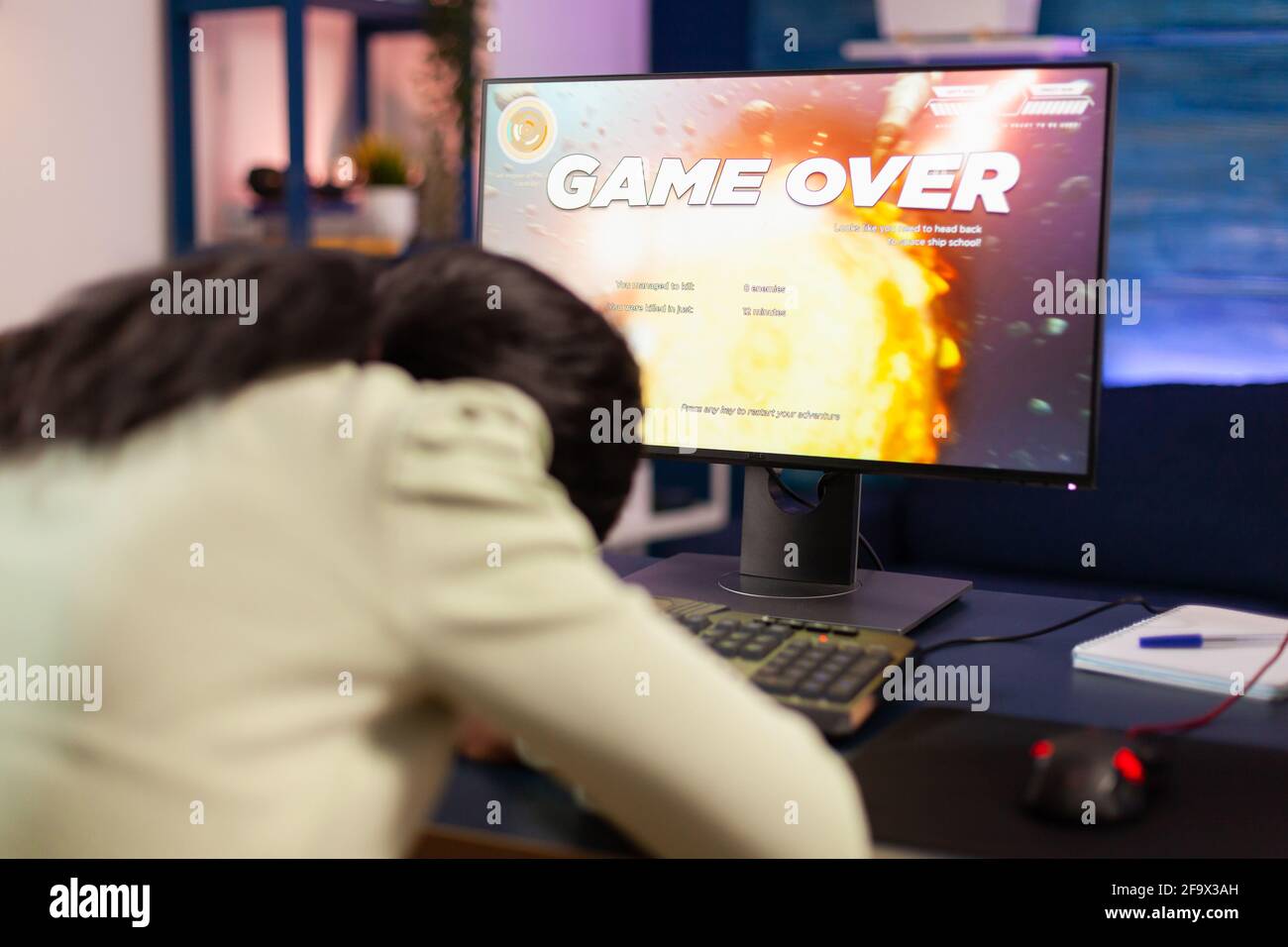 Gamer over for sad african gamer after losing championship sitting with head on the table. Angry professional gamer gaming over during an space shooter online video game. Stock Photo