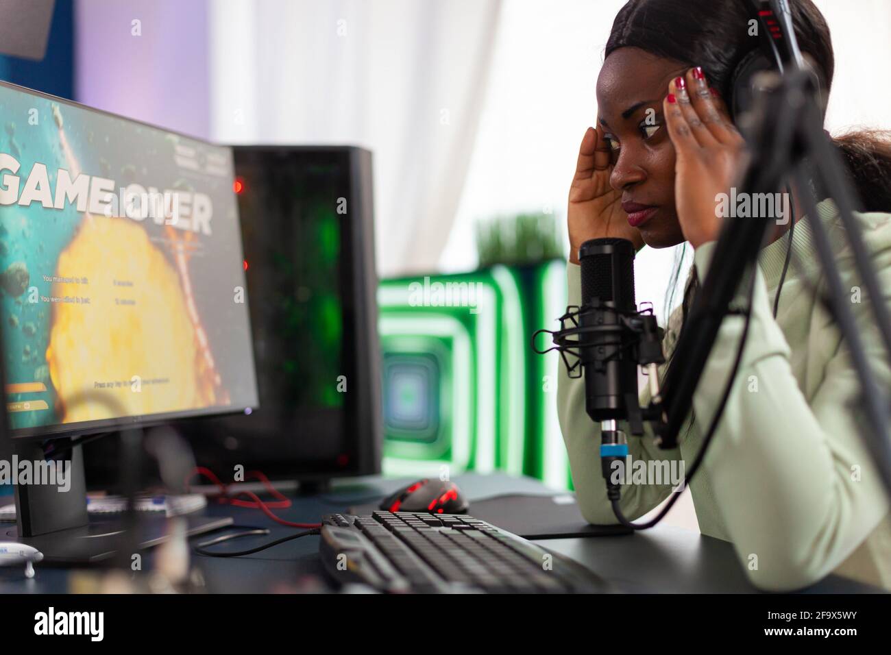 African streamer regrets losing live shooter game tournament touching temple. Professional gamer streaming online video games with new graphics on powerful computer. Stock Photo