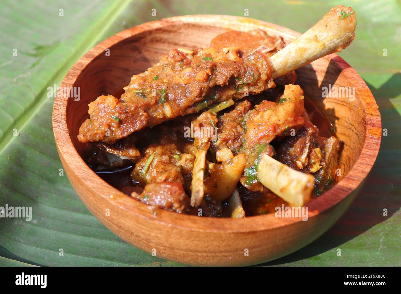 Mutton chops curry. Indian rustic spicy non-vegetarian goat meat curry. served in a wooden bowl over a Banana leaf background. copy space. Stock Photo