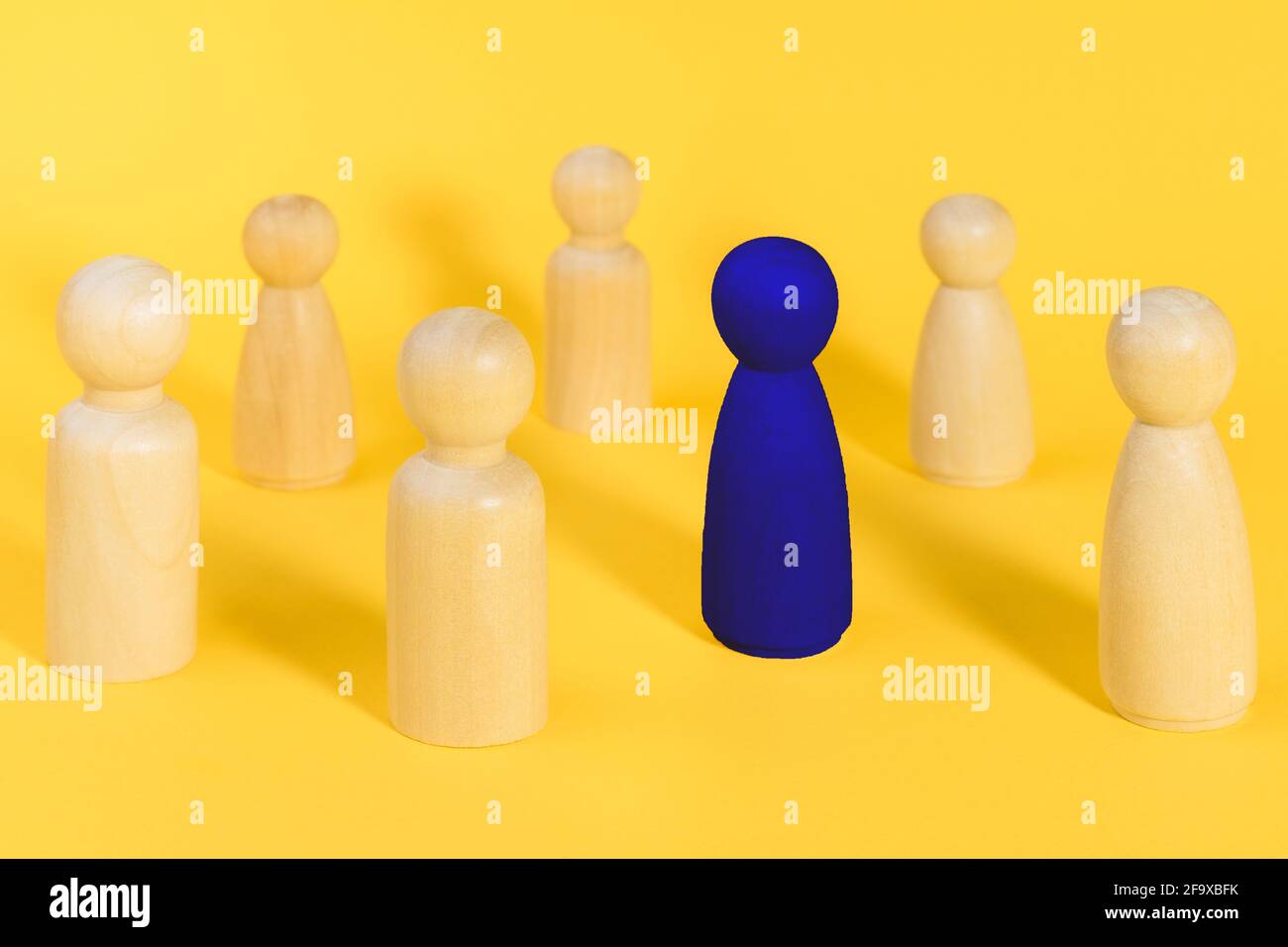Blue wooden figure among many yellow figures. Standing out from crowd ...