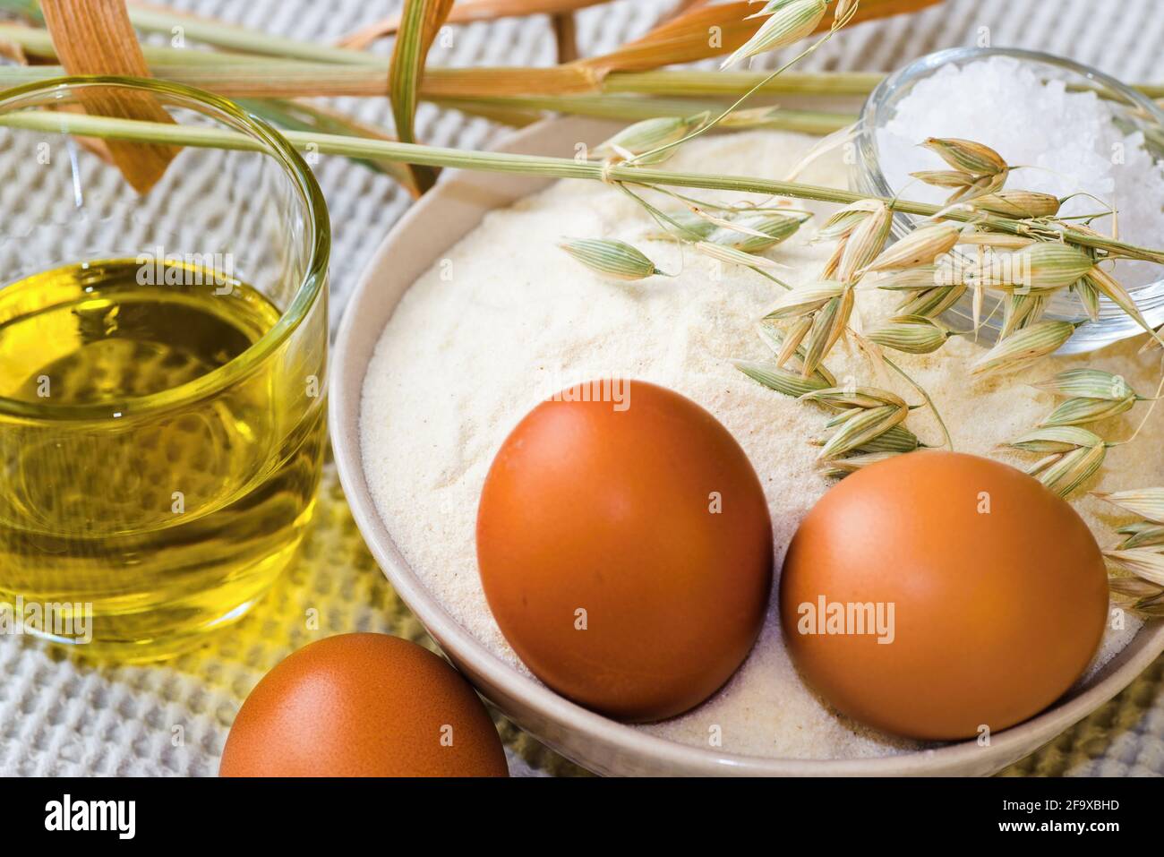 Food ingredients for baking, flour, eggs, oil and ears of corn on white table-cloth on table. Stock Photo