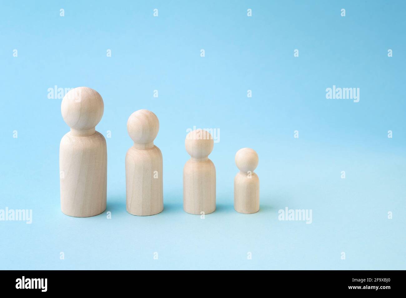 Wooden figurines standing in line from high to low on blue background. Family members or personal Stock Photo