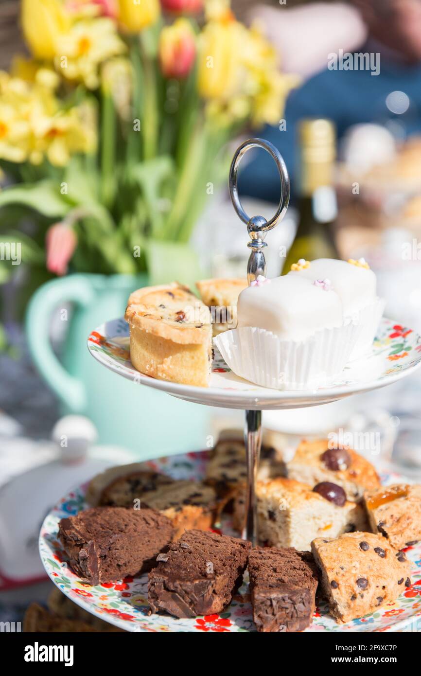 English afternoon tea with cake and sandwiches on a tiered cake stand in a floral garden on a beautiful sunny day Stock Photo