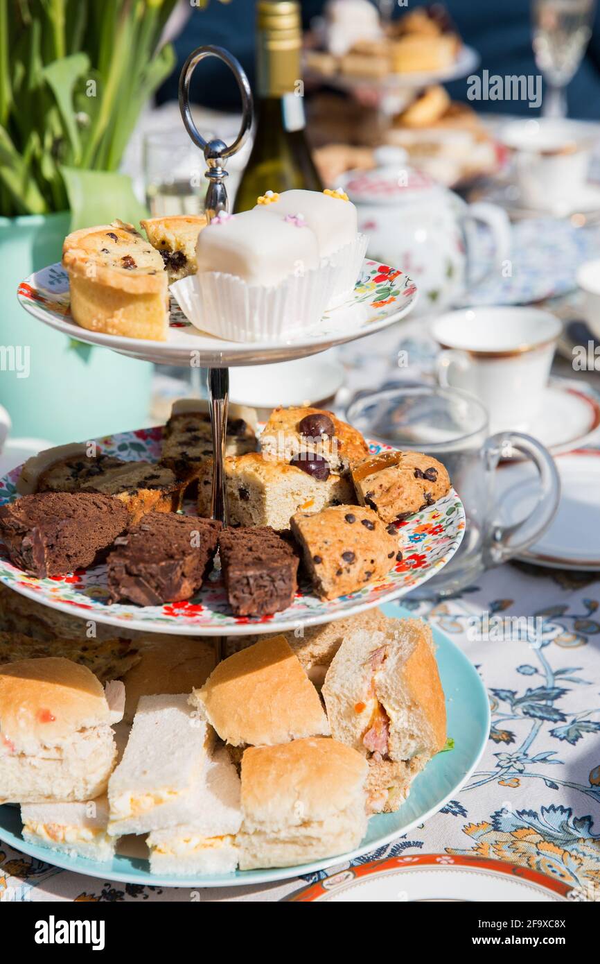English afternoon tea with cake and sandwiches on a tiered cake stand in a floral garden on a beautiful sunny day Stock Photo