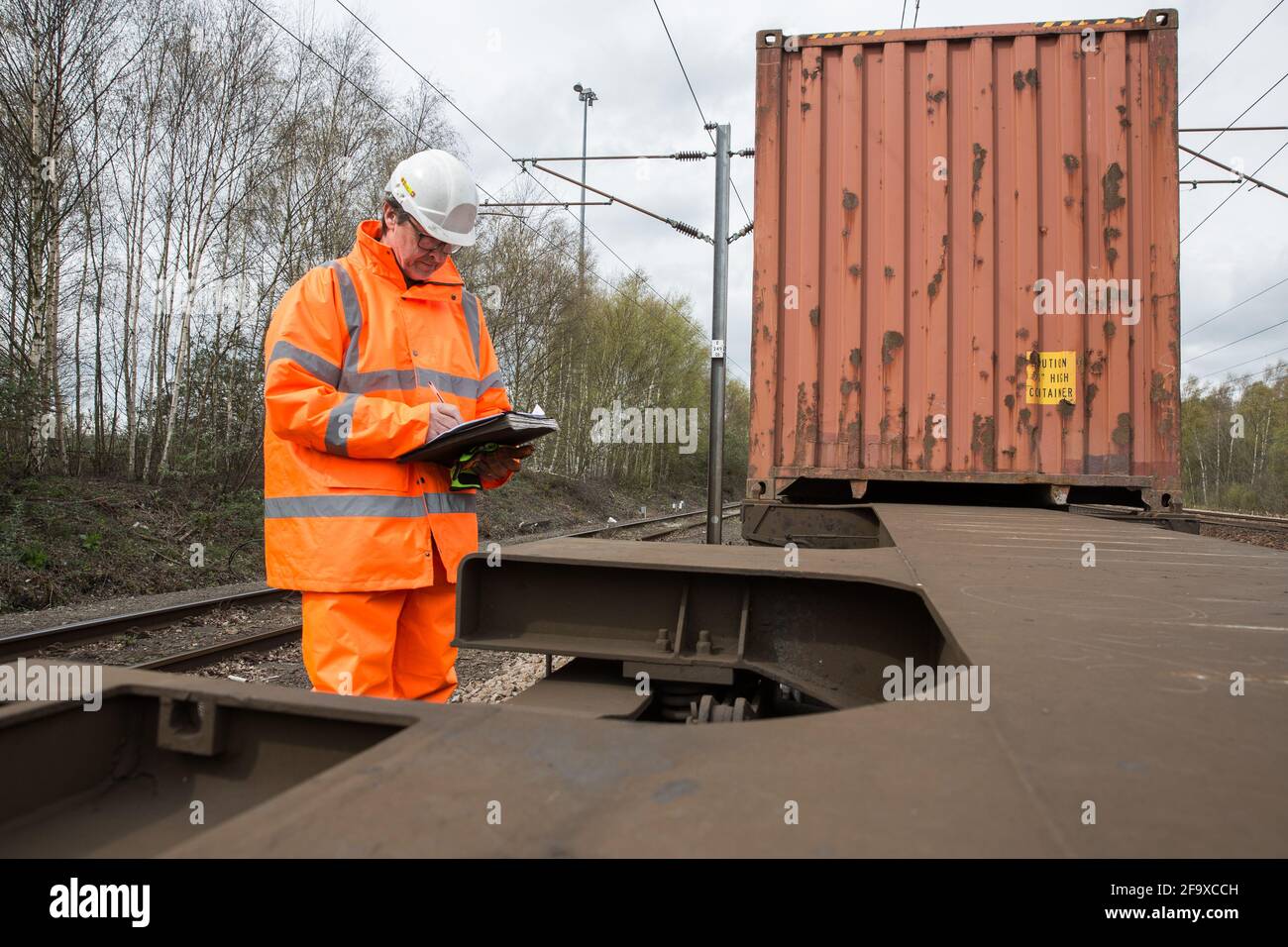 A railway worker in full pipe inspecting and maintaining a shipping container freight train in the UK Stock Photo