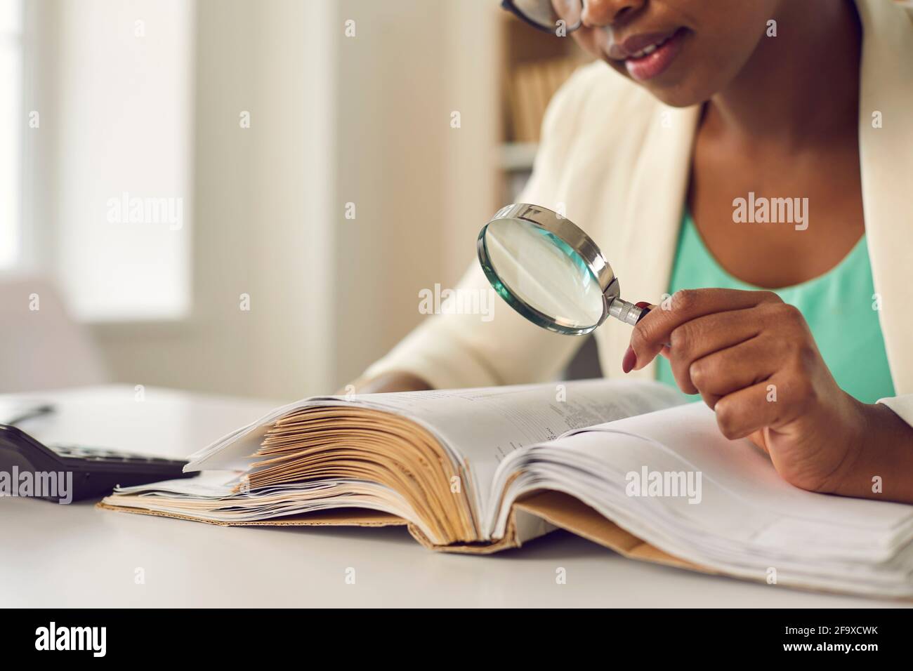 African american woman skeptically looking via magnifying glass at document Stock Photo