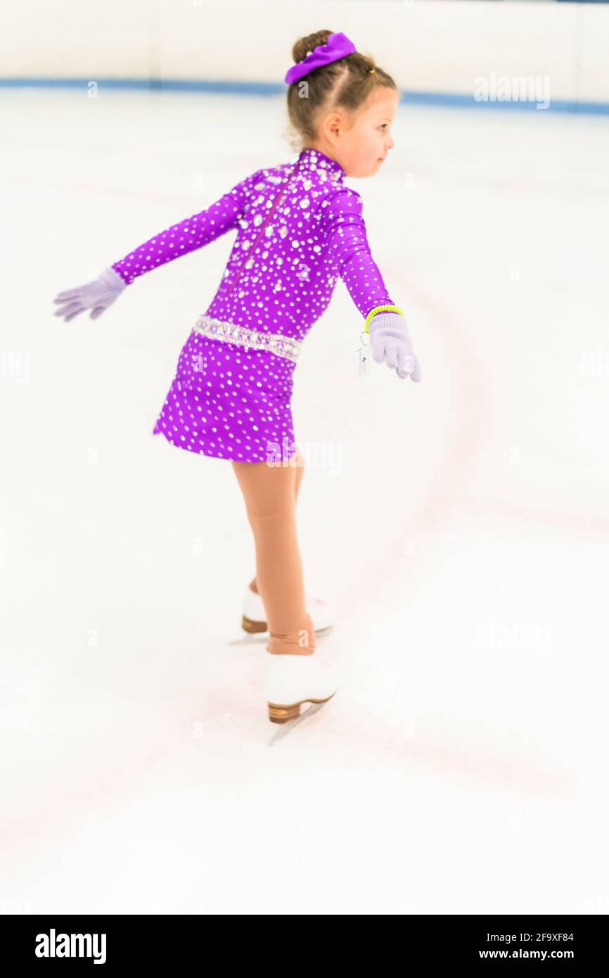 Little girl practicing figure skating in a purple dress with crystals