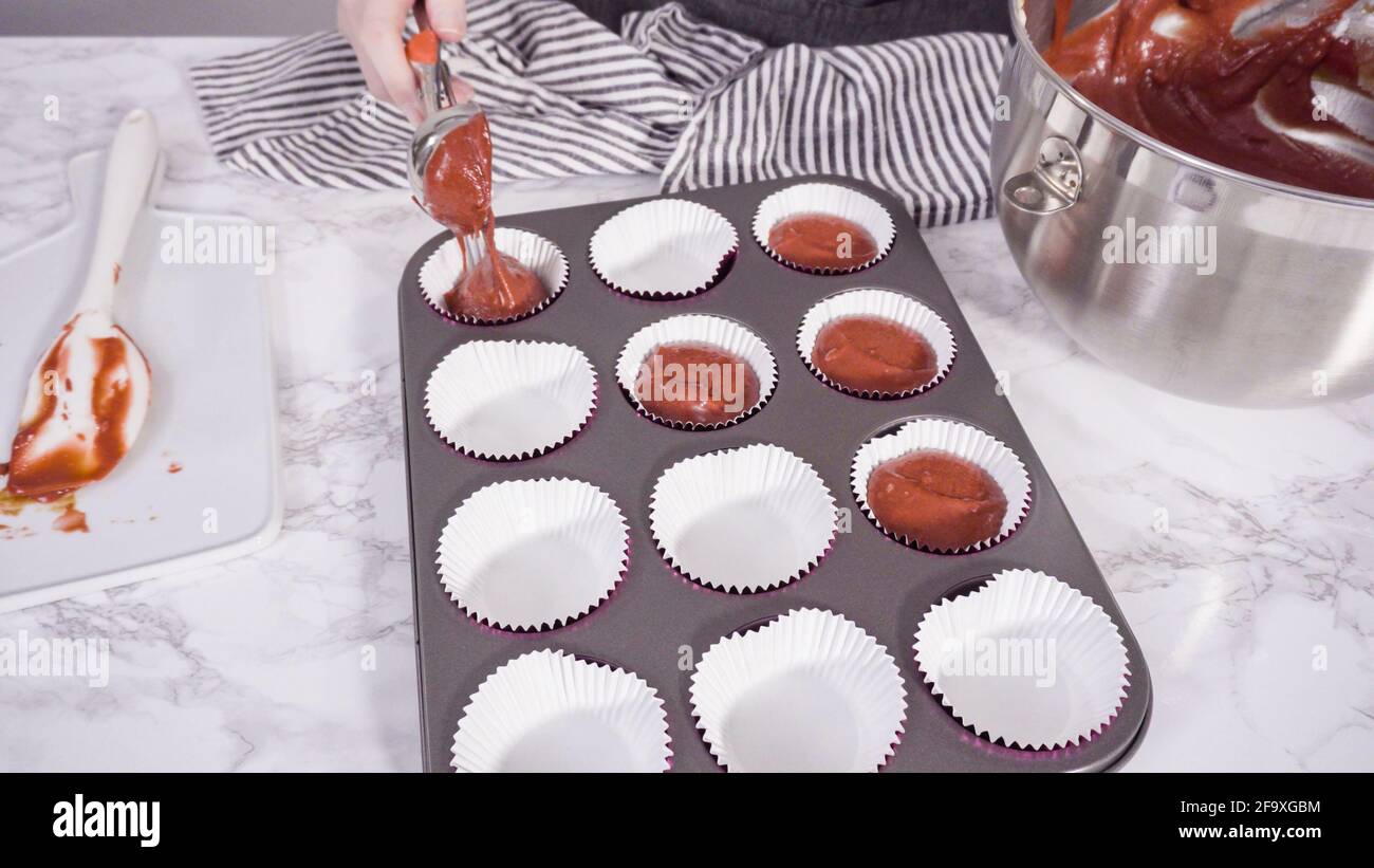 Step by step. Scooping cupcake batter into foil cupcake cups to bake red velvet cupcakes Stock