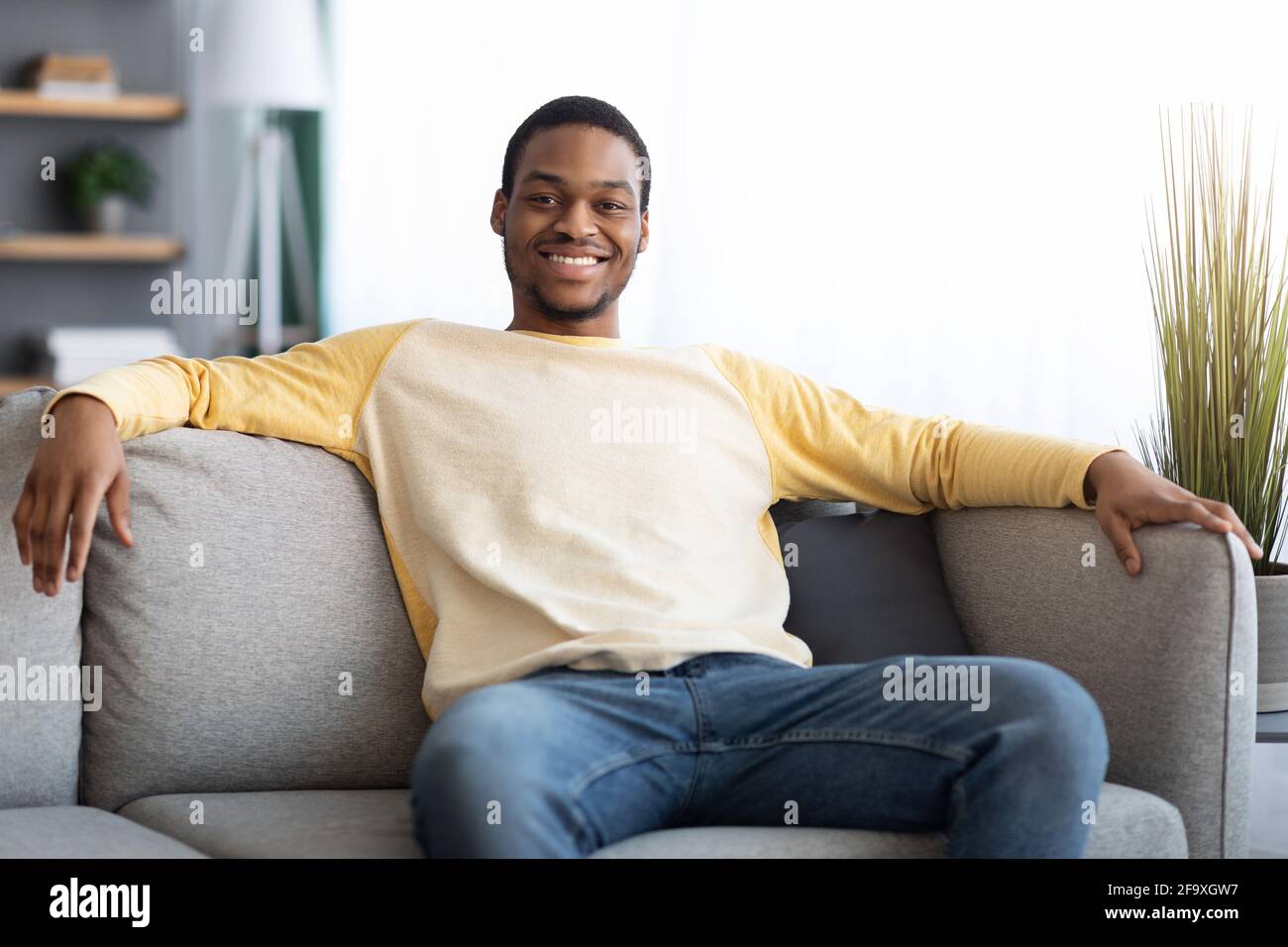 Happy black man sitting on sofa at home Stock Photo - Alamy