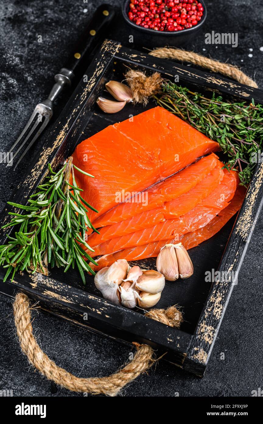 Smoked sliced salmon fillet in a wooden tray with herbs. Black ...
