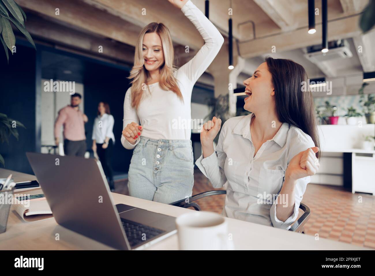 Two young happy businesswomen celebrating project success in office ...