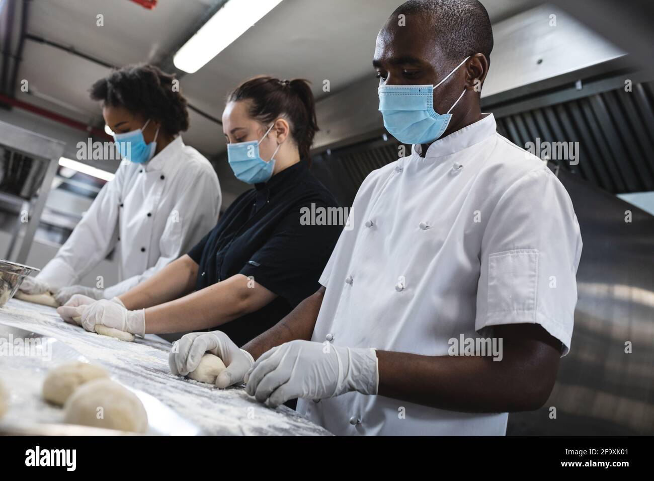 Mixed race professional chefs preparing dough wearing sanitary gloves