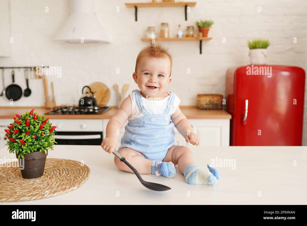 Cute child baby boy 1 years old sitting on the table with big spoon in the kitchen room Stock Photo