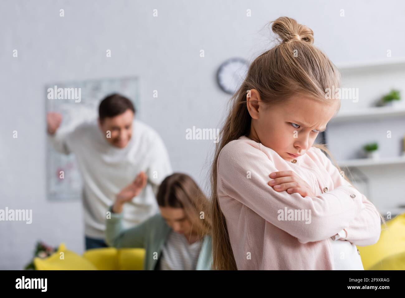Angry kid standing near parents quarrelling on blurred background Stock Photo