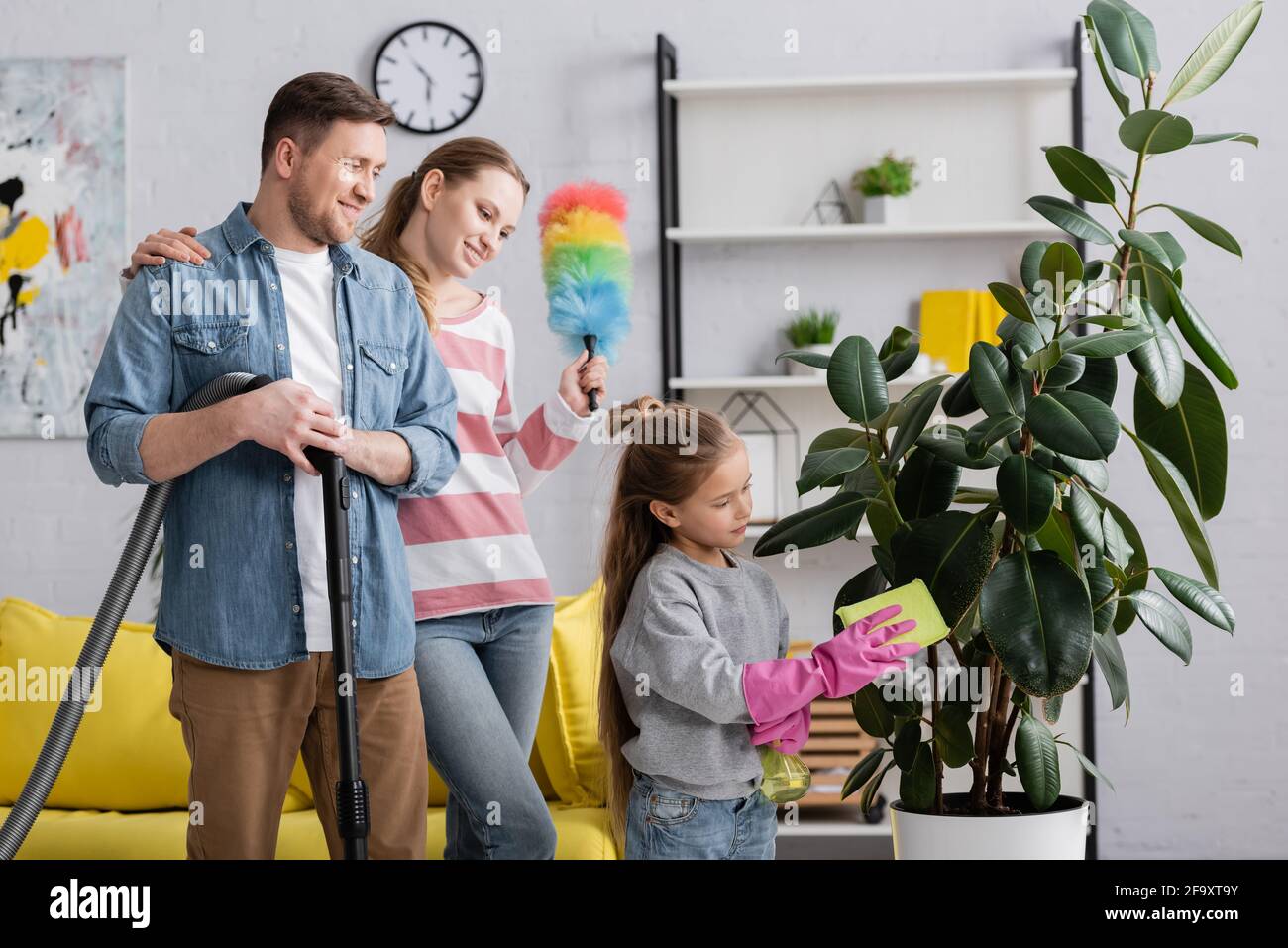 Child cleaning leaves of plant near smiling parents at home Stock Photo