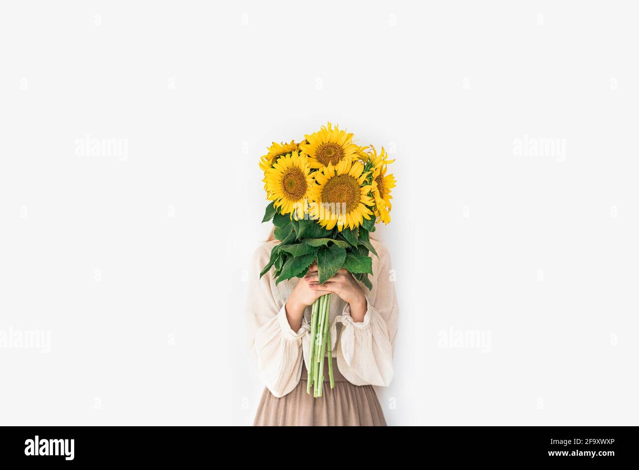 Beautiful young woman in linen dress holding sunflowers bouquet on white background. Autumn concept. Stock Photo