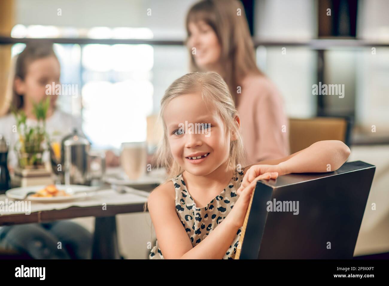 Sweet girl sitting at the table in the restaurant with family Stock Photo