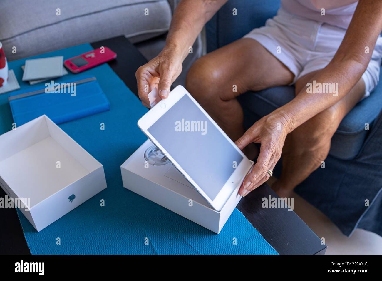 Older woman unboxing a new Apple ipad mini tablet in her living room. Stock Photo