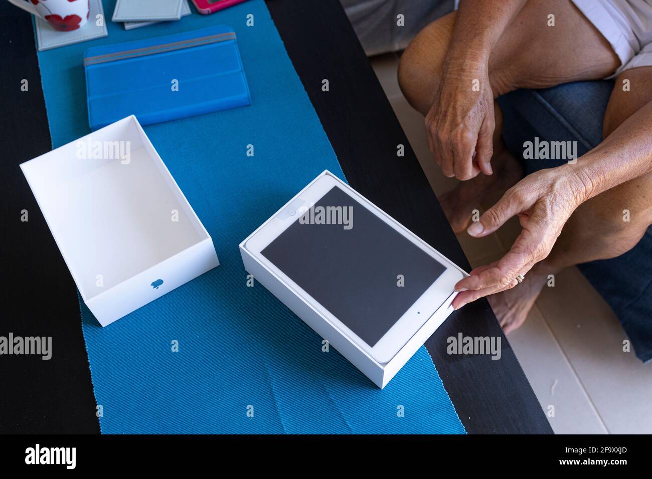 Older woman unboxing a new Apple ipad mini tablet in her living room. Stock Photo