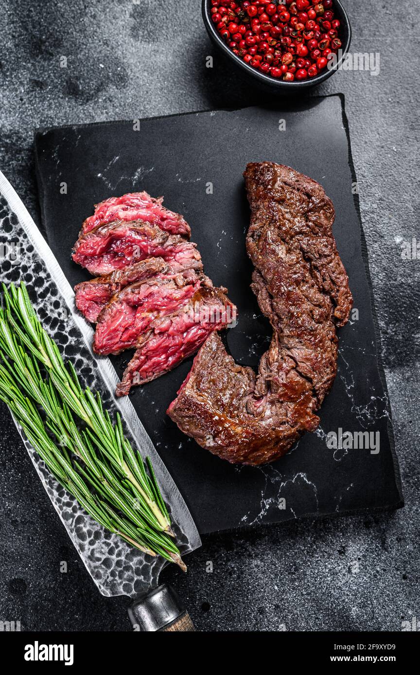 Sliced grilled Onglet Hanging Tender steak on a marble board. Black background. Top view Stock Photo