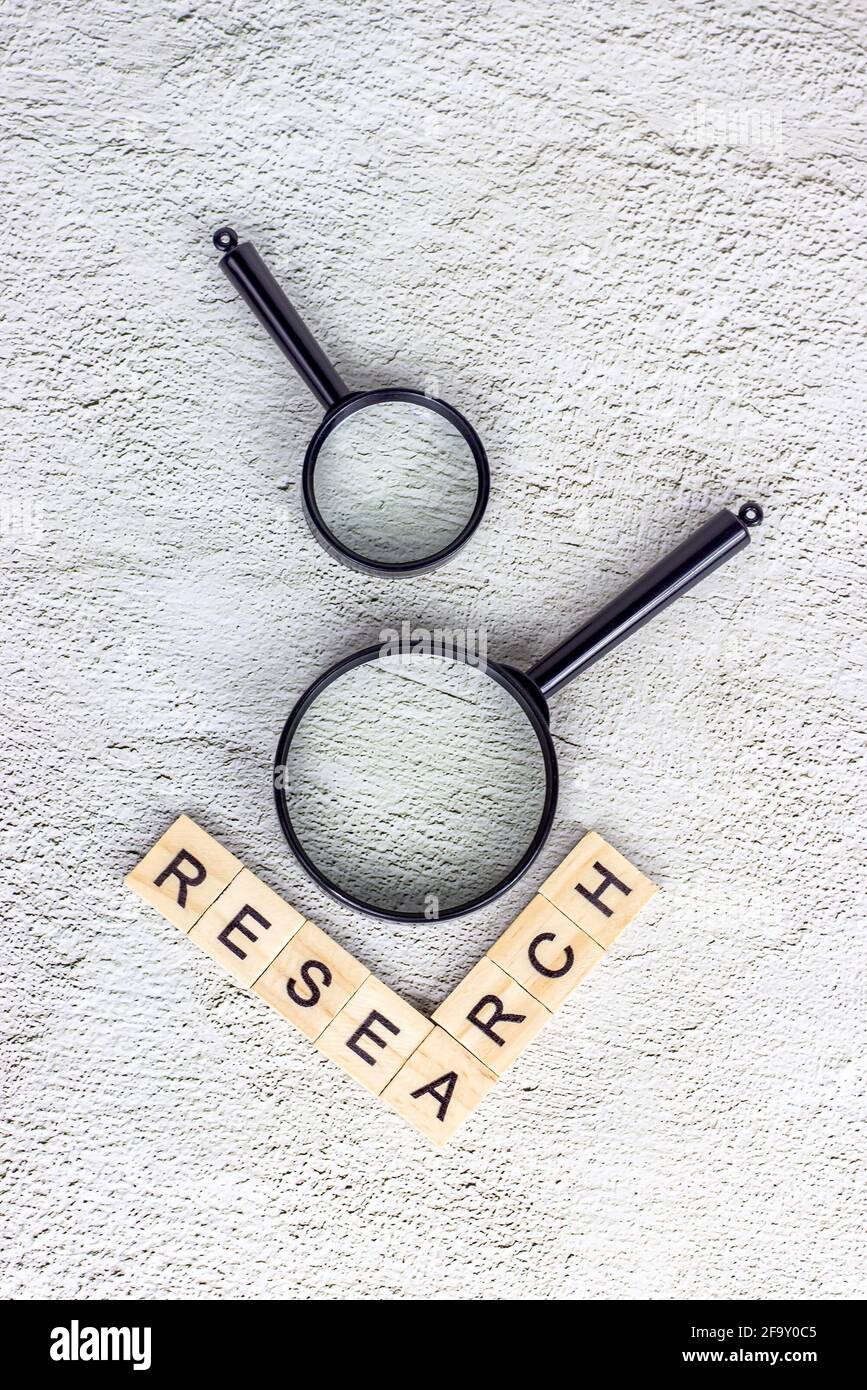 Black magnifying glass with research text on light gray background. Statistic analyzing and scientific search concept. Stock Photo