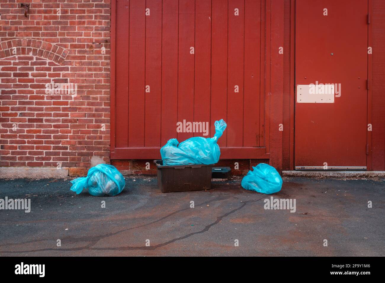 Three bright blue plastic garbage/trash bags in alley behind restaurant. Stock Photo
