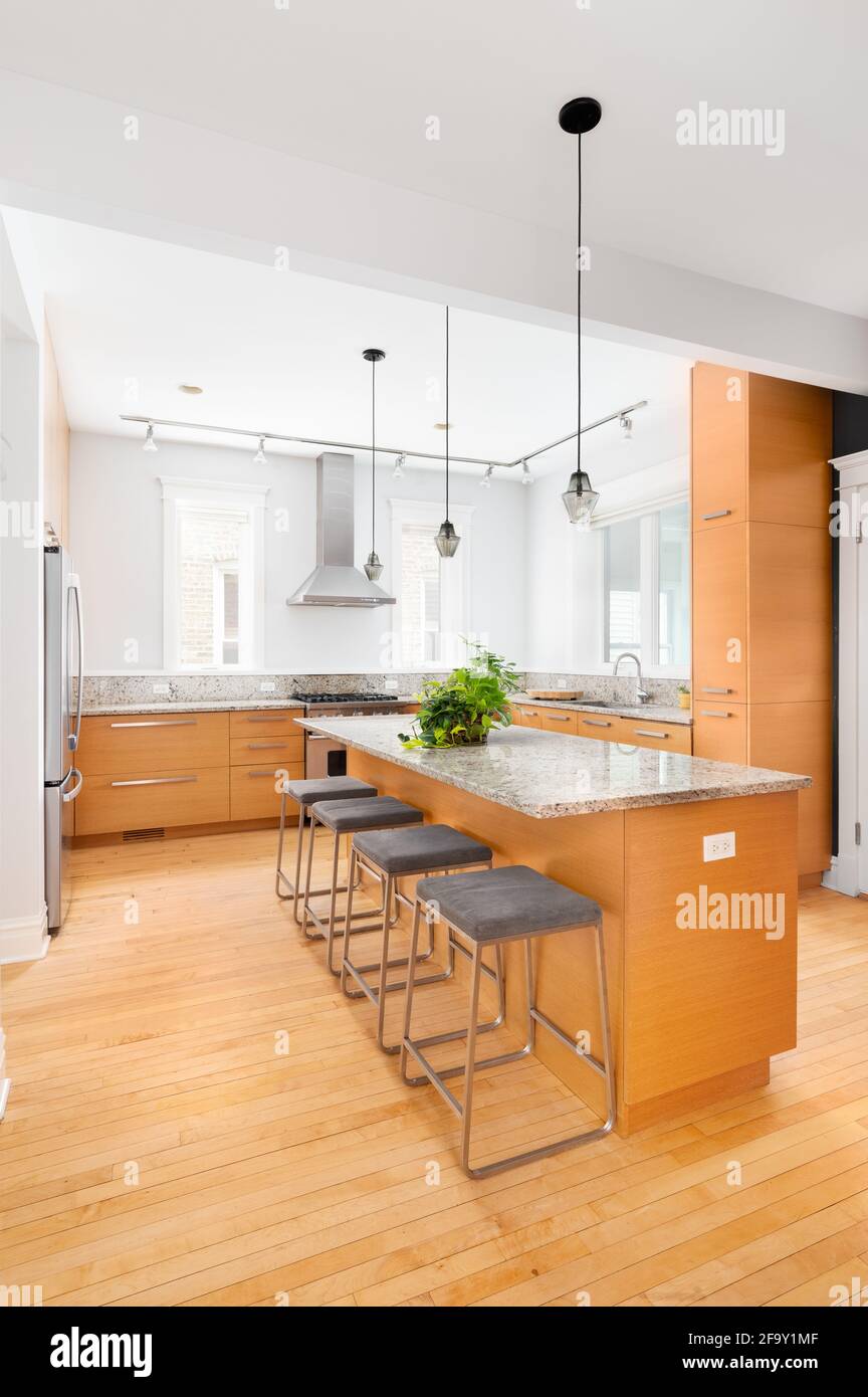 A luxury kitchen with light wood cabinets, a large island with bar stools, stainless steel Viking appliances, and a granite countertop. Stock Photo