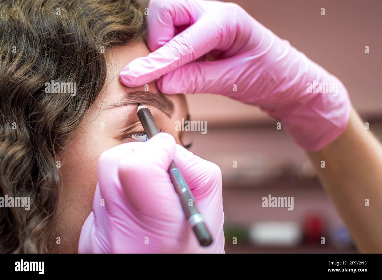 eyebrow master draws the shape of the eyebrows of a young woman with an
