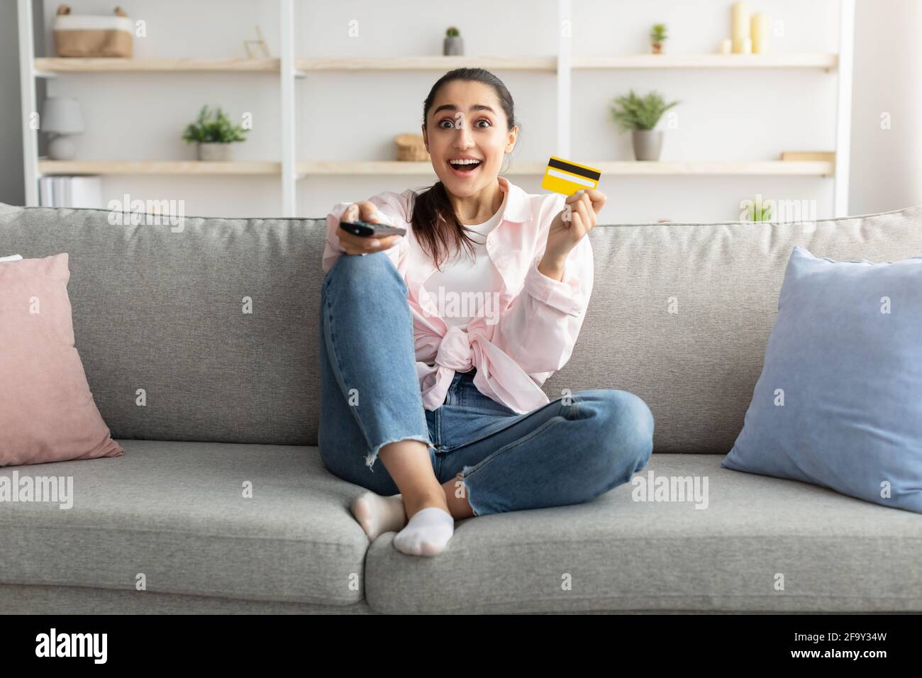 Excited woman holding remote control and debit credit card Stock Photo