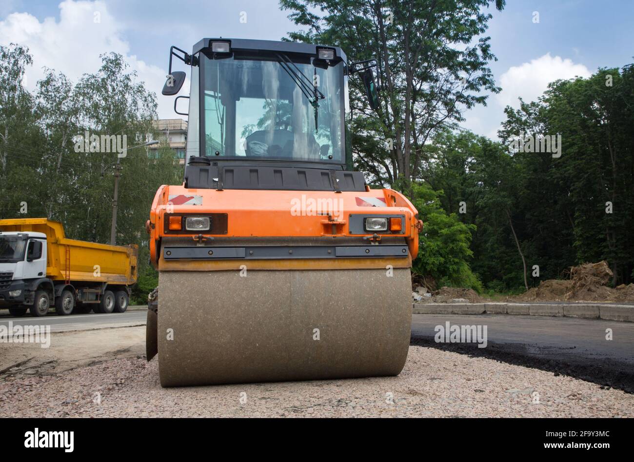 large orange roller on road paving works. In the background is a dump  truck. Improvement of the city. Equipment for road construction and repair  Stock Photo - Alamy