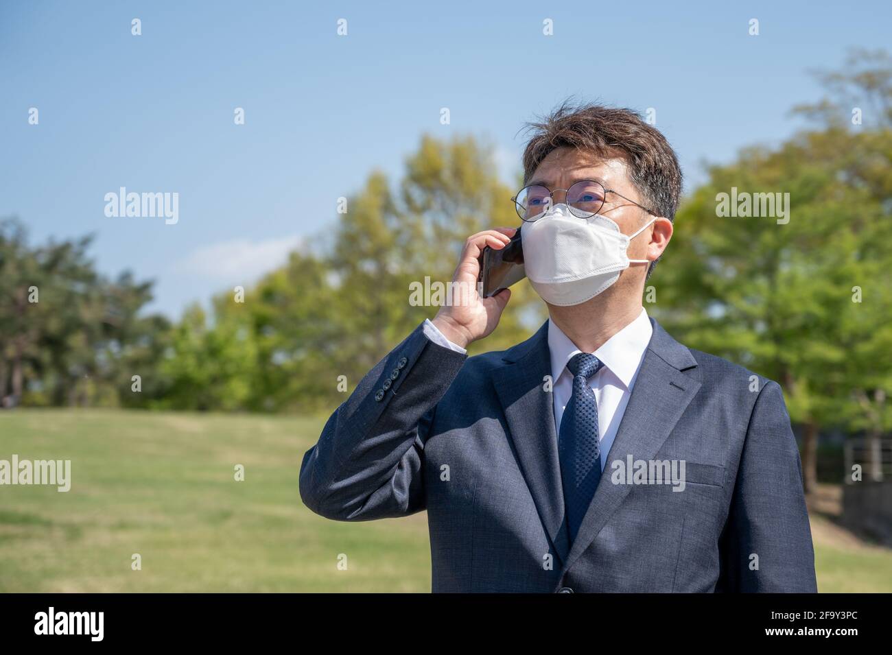 Middle-aged Asian businessman wearing a mask and using a smartphone on the lawn. Stock Photo