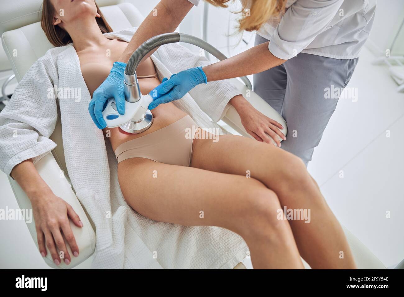 Unrecognized woman in white bathrobe receiving Ultrasound cavitation body contouring treatment in wellness clinic Stock Photo