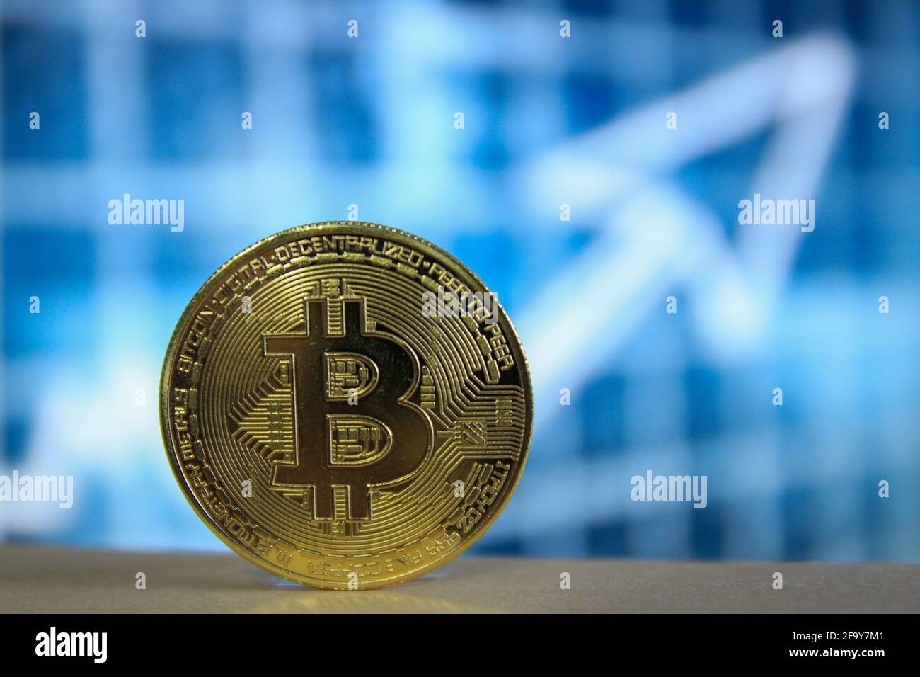 A physical version of Bitcoin BTC with blurred blue background and an arrow. Stock Photo