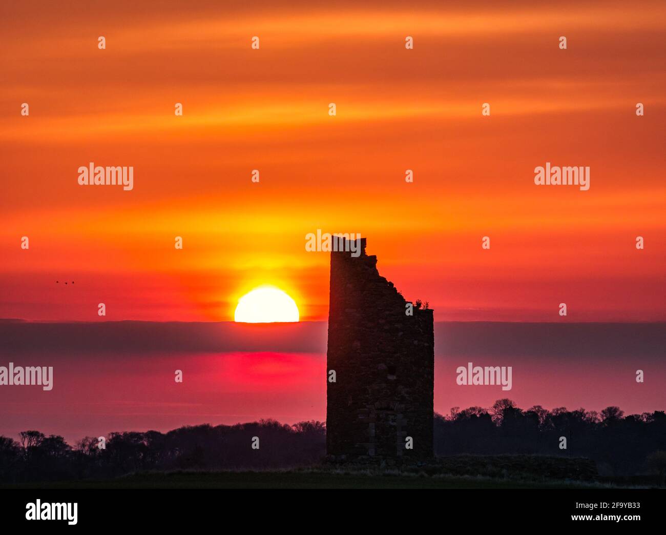 Orange and pink sunrise over ruins of  Balgone Barns windmill tower, East Lothian, Scotland, UK Stock Photo