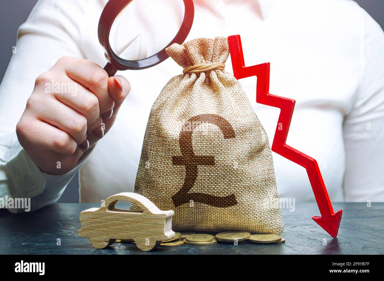 Woman examines a british pounds sterling money bag with a red down arrow and automobile. Car insurance, taxes, maintenance. Fuel excise taxes. Electri Stock Photo
