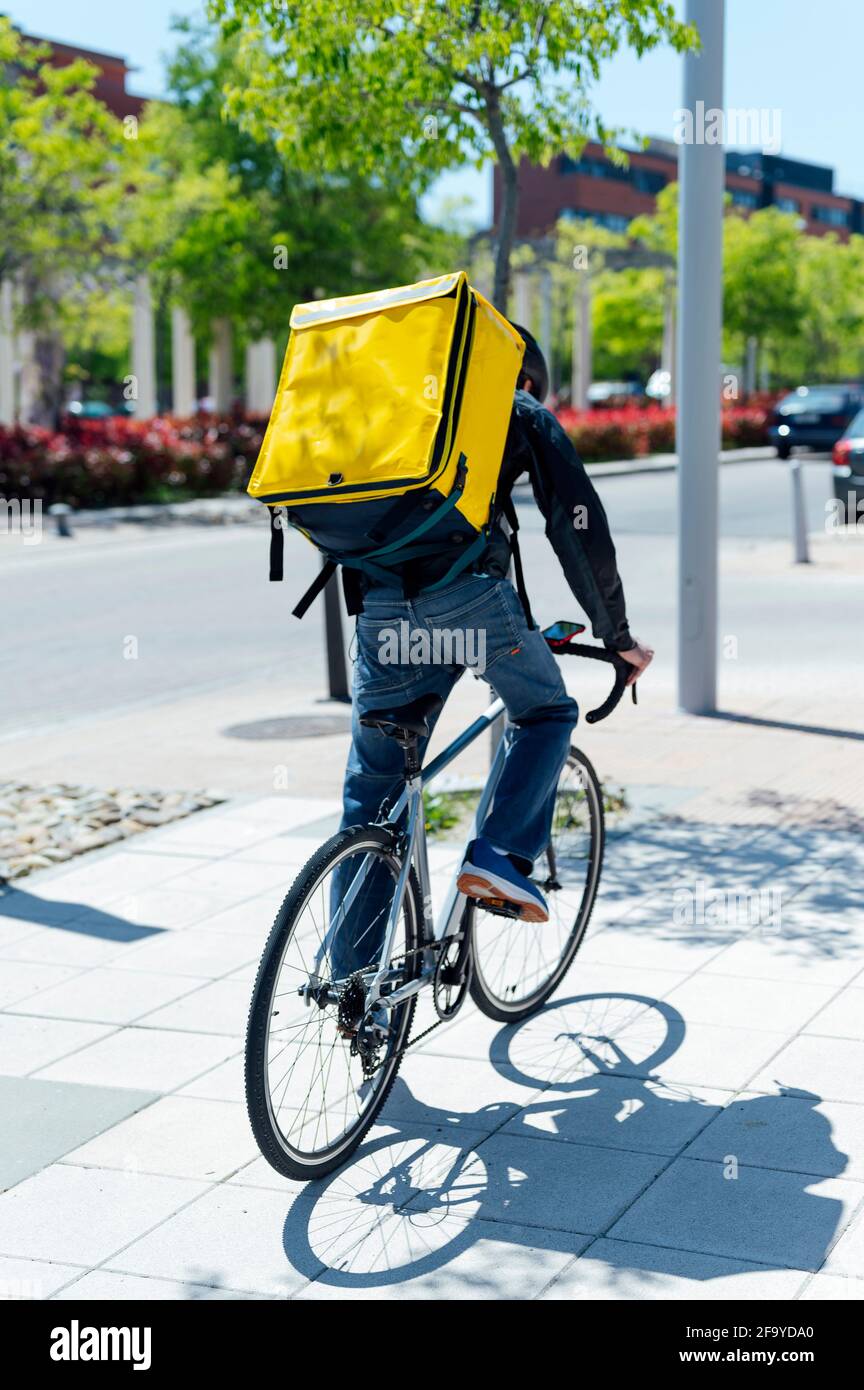 courier delivering food with a yellow thermal backpack, riding a bicycle in the city. Food delivery service concept Stock Photo