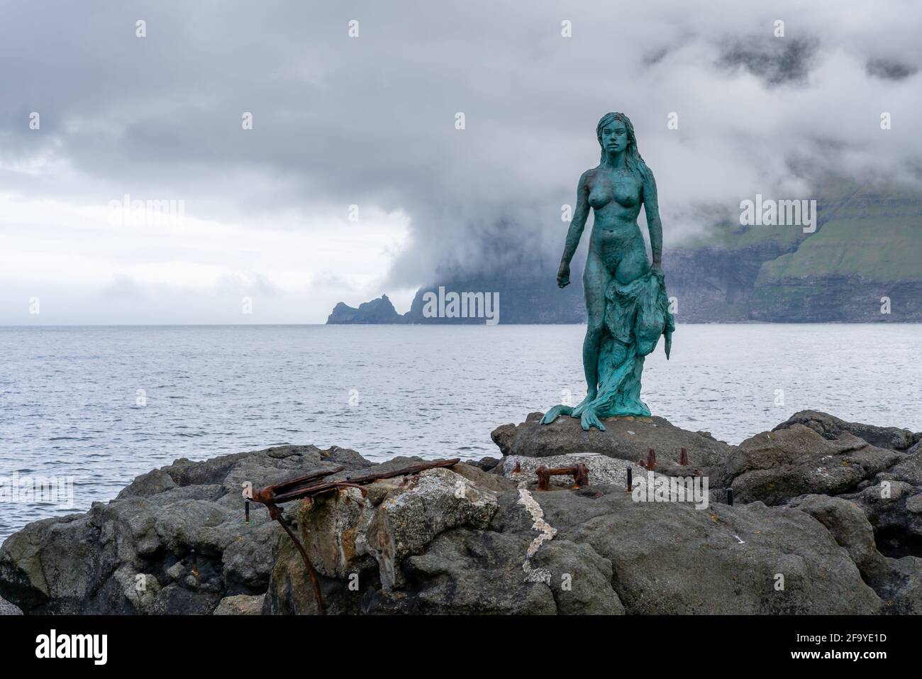 Mikladalur, Faroe Islands - 06.12.2017: Statue of Seal Woman on the rocky shore of Mikladalur, Kalsoy, with ocean anc dramatic clouds in the backgroun Stock Photo