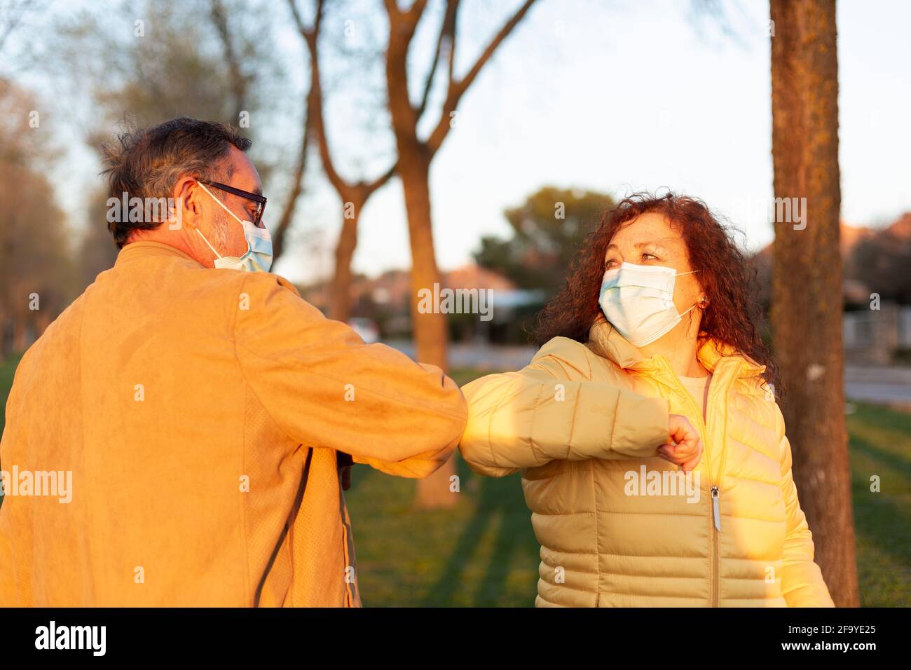 Two older people wearing face masks greet each other with elbows together. Concept of social distancing and new normal. Stock Photo