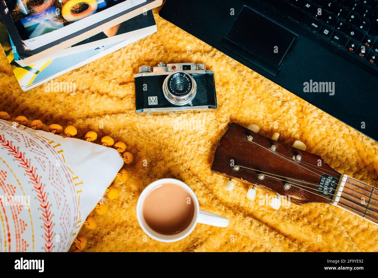 Still life, lay flat of a cosy home scene. A blanket on the floor with a guitar, vintage film camera, books and tea . Creative freelancer lifestyle Stock Photo
