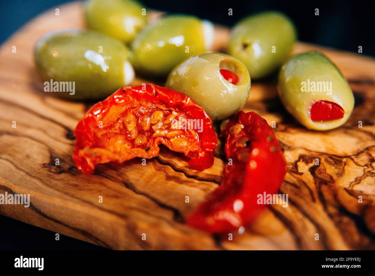 close up of a bamboo wood chopping board with sun dried tomatoes and olives Stock Photo