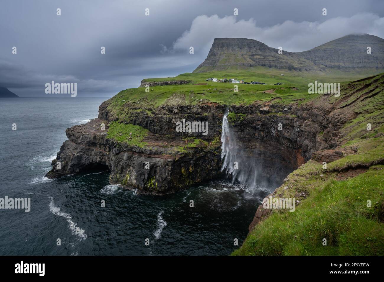 Word famous Mulafossur waterfall falling from the cliff into the ocean in the strong wing. Cloudy, windy  weather in Faroe Islands. Gasadalur village Stock Photo