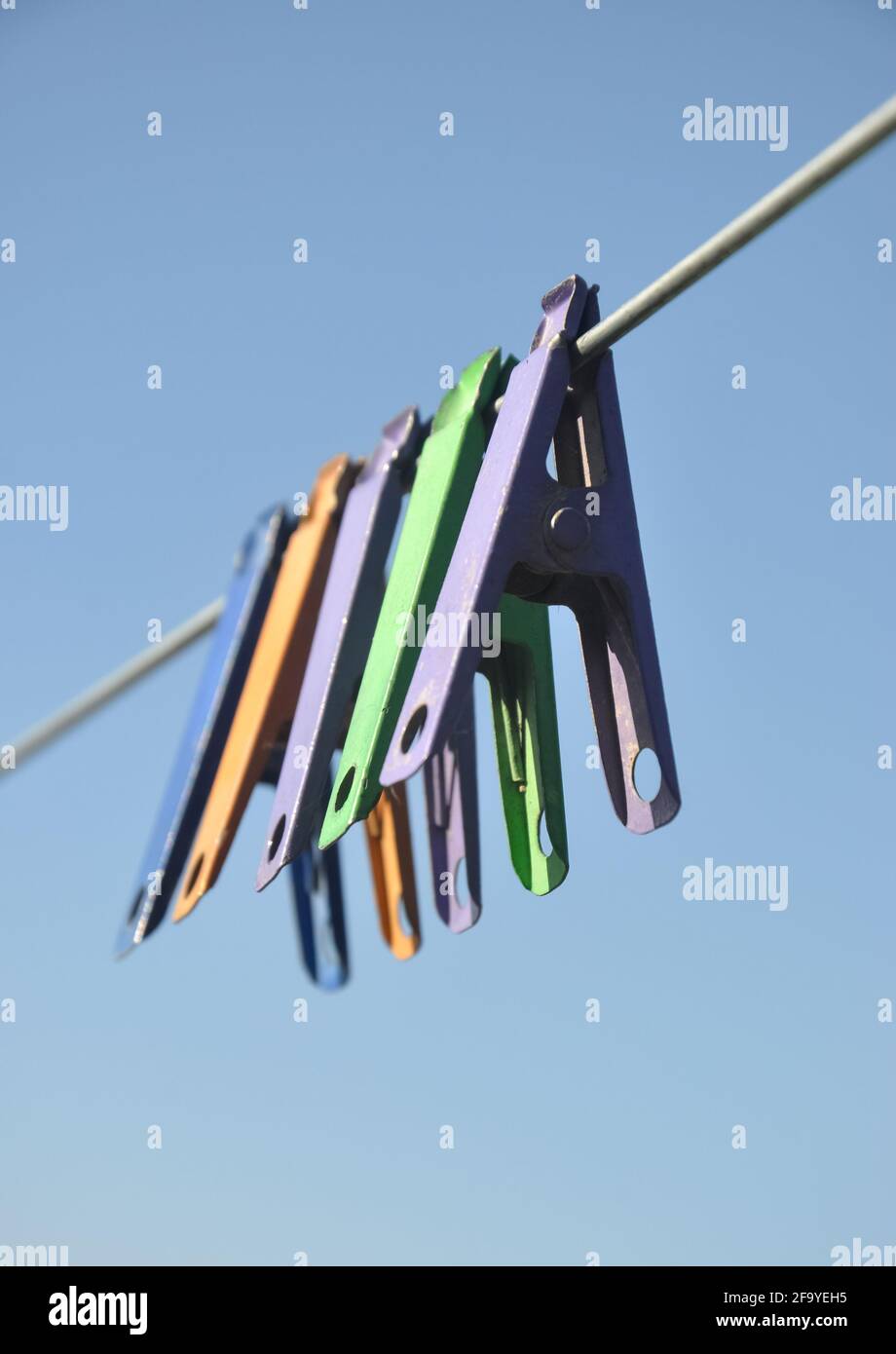 Low angle shot of multicolored cloth pins hanging on wire in outdoor with blue sky in background Stock Photo
