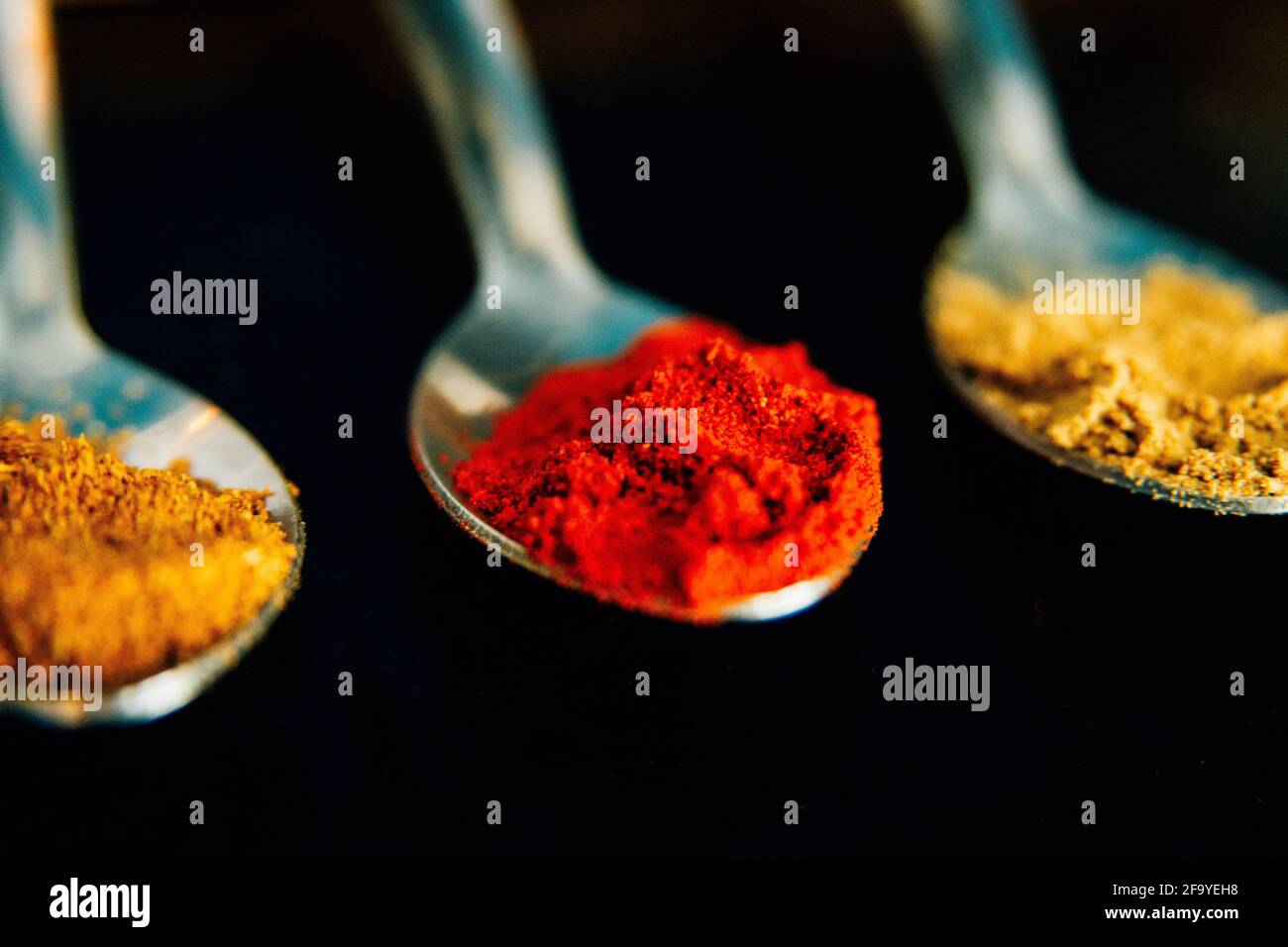 Colourful herbs and spices on silver spoons against a black background. Paprika, Cumin, Ginger. Ingredients for cooking spicy food. Stock Photo