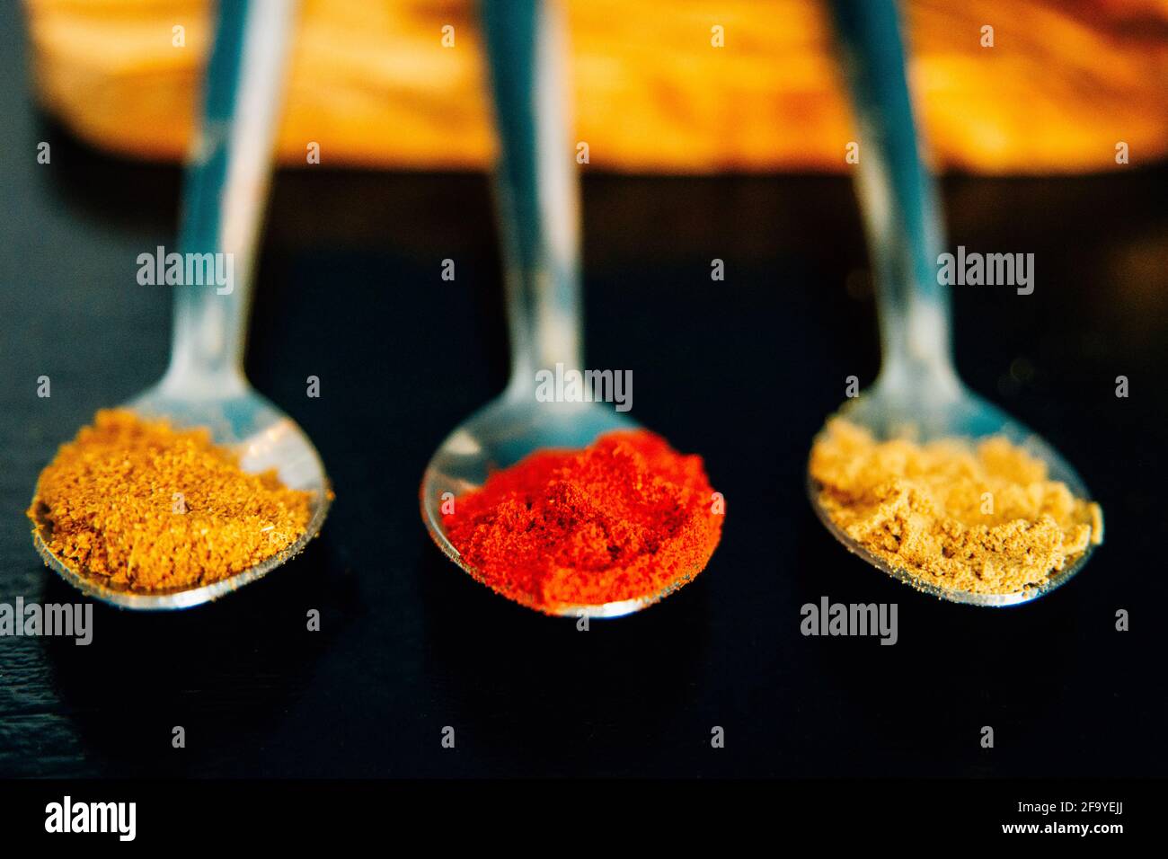 Colourful herbs and spices on silver spoons against a black background. Paprika, Cumin, Ginger. Ingredients for cooking spicy food Stock Photo