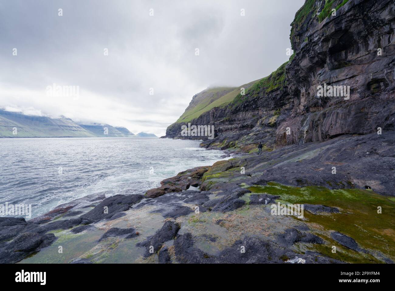 Rocky Faroese shore on a cloudy day. Cliffs of Kalsoy island. Late cloudy morning in the wild fjords of Faroe Islands near the Mikladalur village. Stock Photo