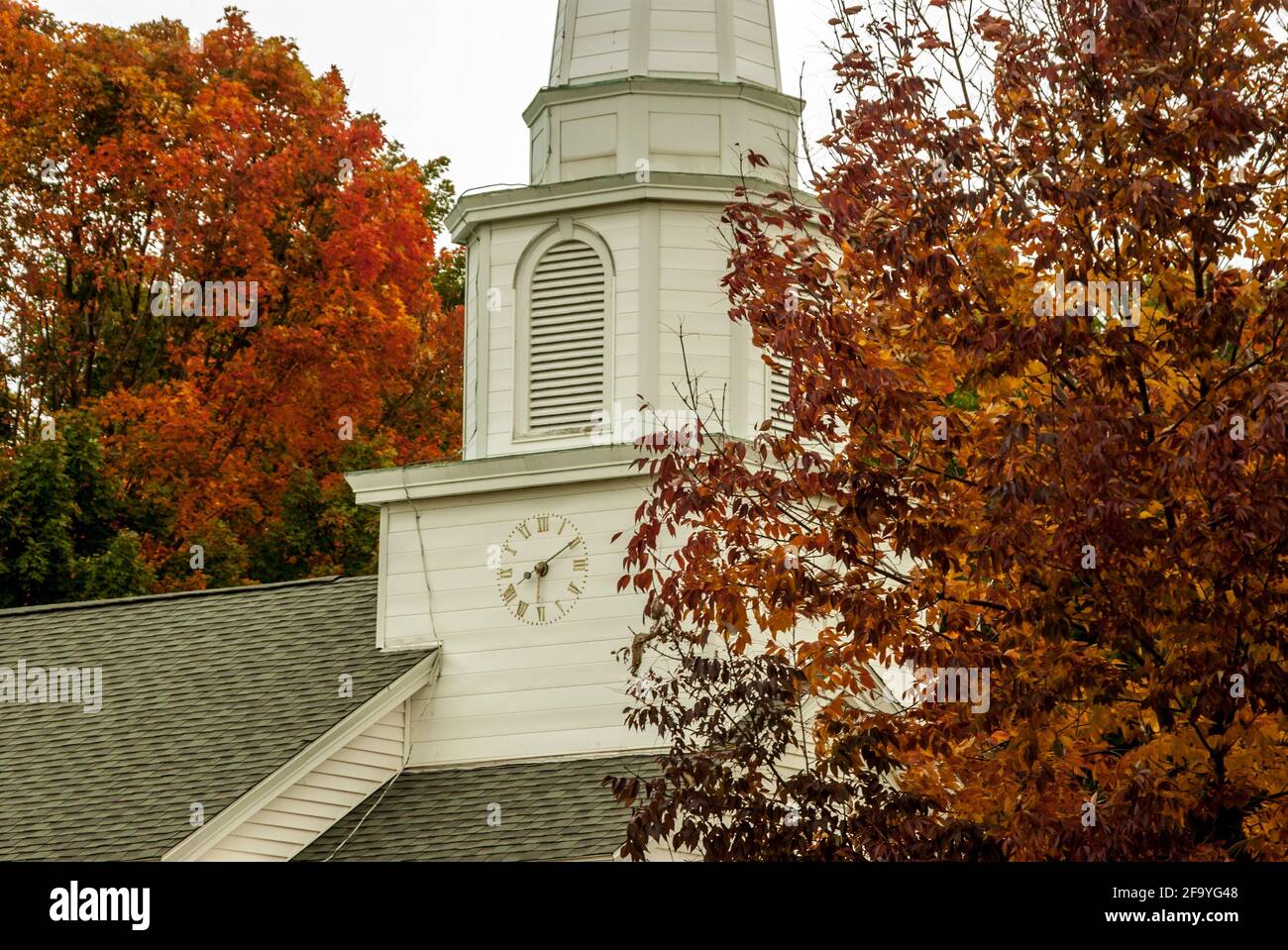 The white, wooden clock tower of Canterbury United Community Church, New Hampshire, USA amongst red foliage in autumn / fall Stock Photo