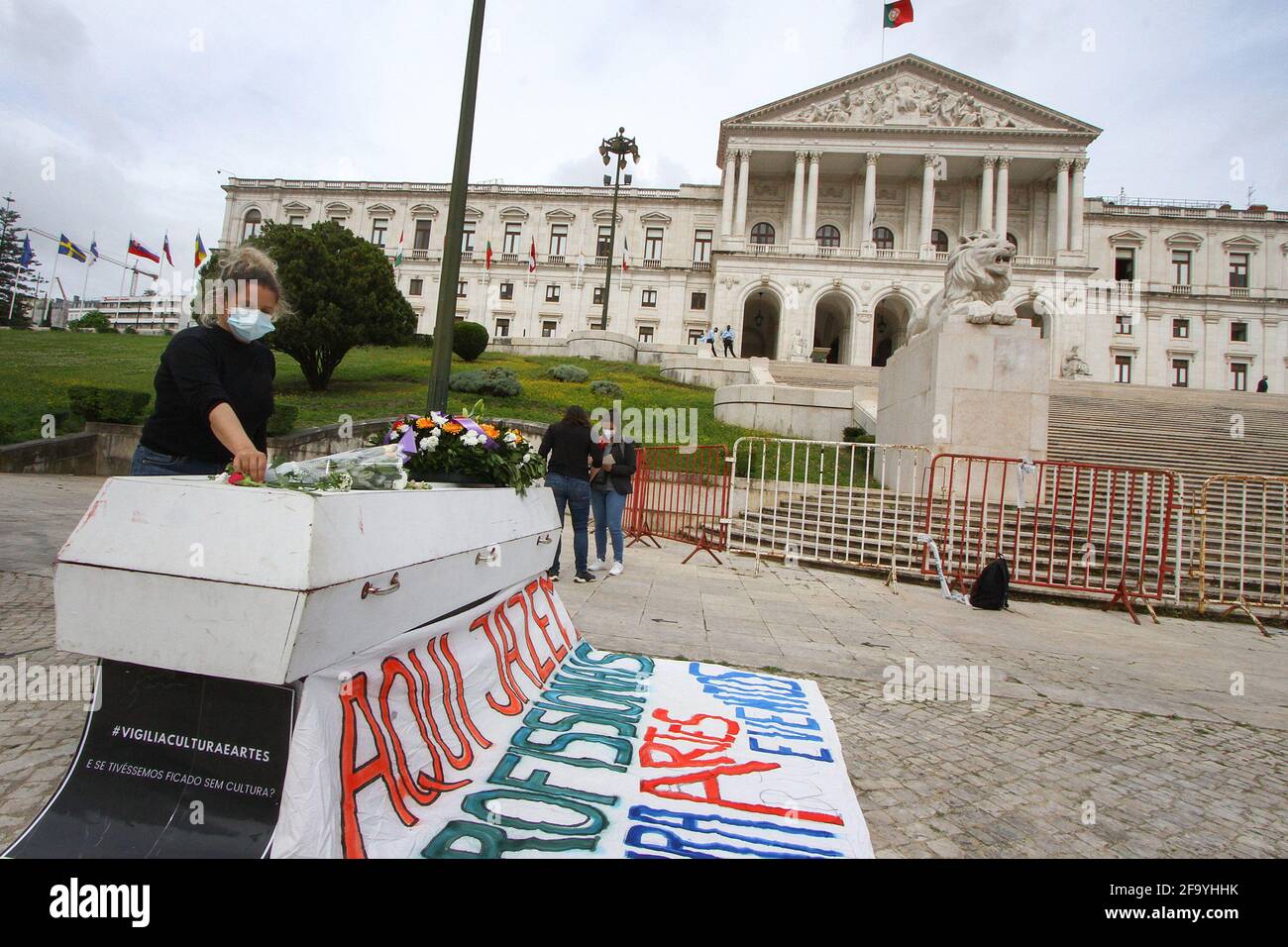 Lisbon, Portugal. 21st Apr, 2021. A woman wearing a protective mask places flowers on top of a coffin during a funeral outside the Republic Assembly palace in Lisbon.The 'Vigília Cultura e Artes' group performs a street protest in order to keep vigil for all the professionals of the culture sector who have been left behind by the few emergency measures programmed by the Portuguese Government in the face of the COVID-19 pandemic. Credit: SOPA Images Limited/Alamy Live News Stock Photo