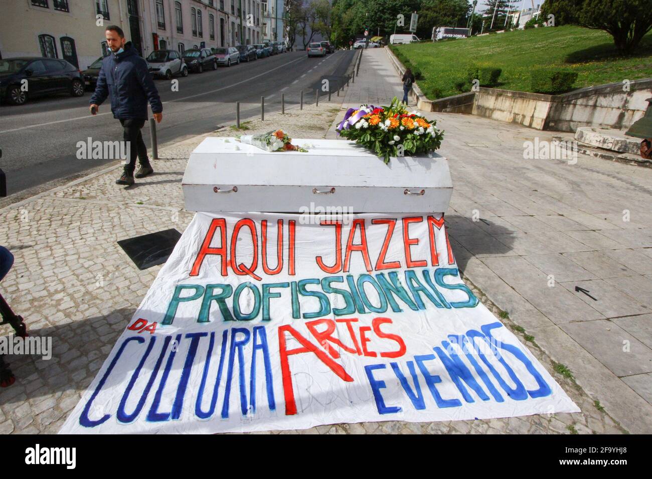 Lisbon, Portugal. 21st Apr, 2021. A man walks near a coffin simulating a funeral ceremony outside the Republic Assembly Palace in Lisbon. The 'Vigília Cultura e Artes' group performs a street protest in order to keep vigil for all the professionals of the culture sector who have been left behind by the few emergency measures programmed by the Portuguese Government in the face of the COVID-19 pandemic. Credit: SOPA Images Limited/Alamy Live News Stock Photo